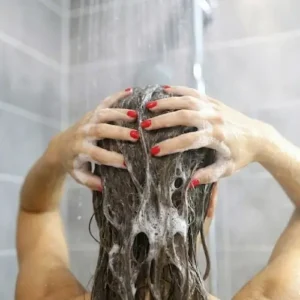 Femme sous la douche massant son cuir chevelu sensible avec la mousse du shampoing doux Celesta Skincare, formulé sans sulfate, sans silicone, sans paraben ni parfum