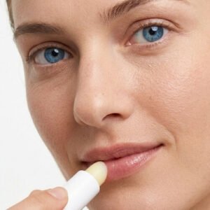 Gros plan d'une femme aux yeux bleus appliquant le baume à lèvres hydratant Celesta Skincare sur ses lèvres pour traiter la sécheresse cutanée.